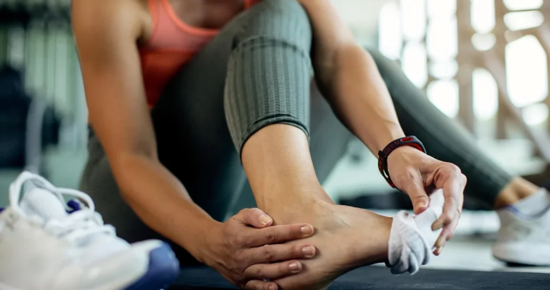 A woman is tying her shoe using her foot while sitting on a bench.