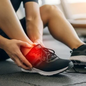 A man grimaces while holding his injured ankle, indicating pain and discomfort.