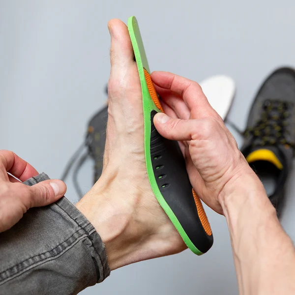 A person is inserting a shoe insert into a shoe before putting it on their foot.