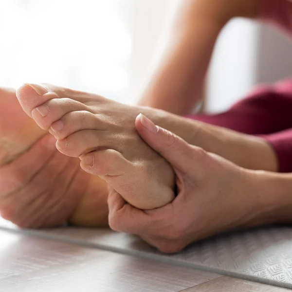 A woman is seated on a yoga mat, holding her foot while practicing a yoga pose.