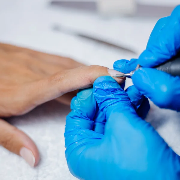 A person receiving a manicure while a nail technician wears blue gloves.